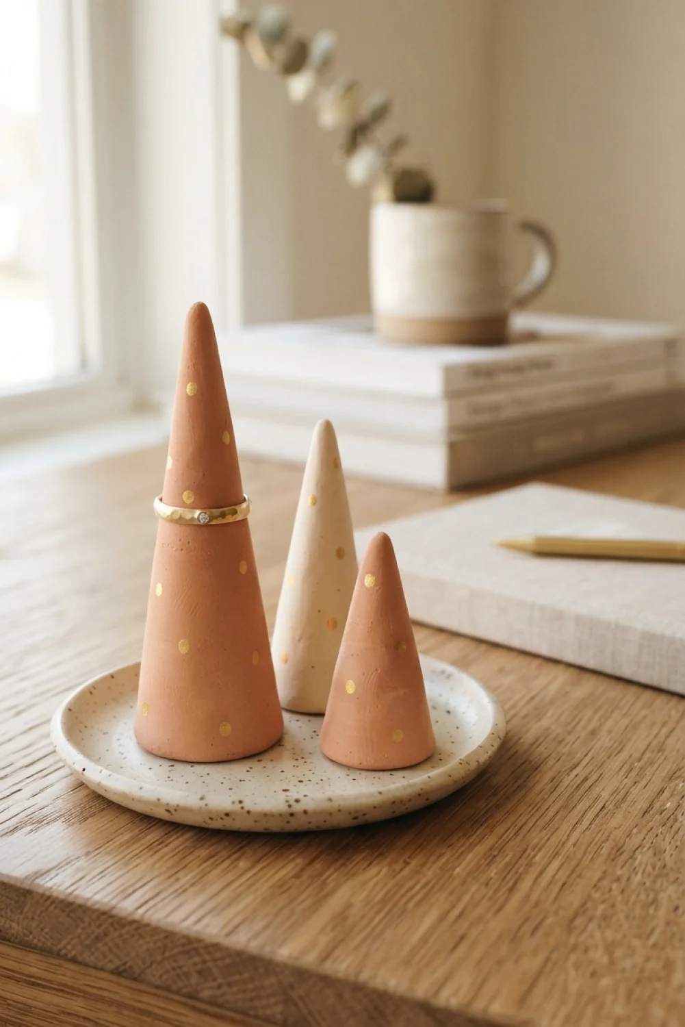 Three terracotta and cream air dry clay cone ring holders with gold dots on a speckled plate