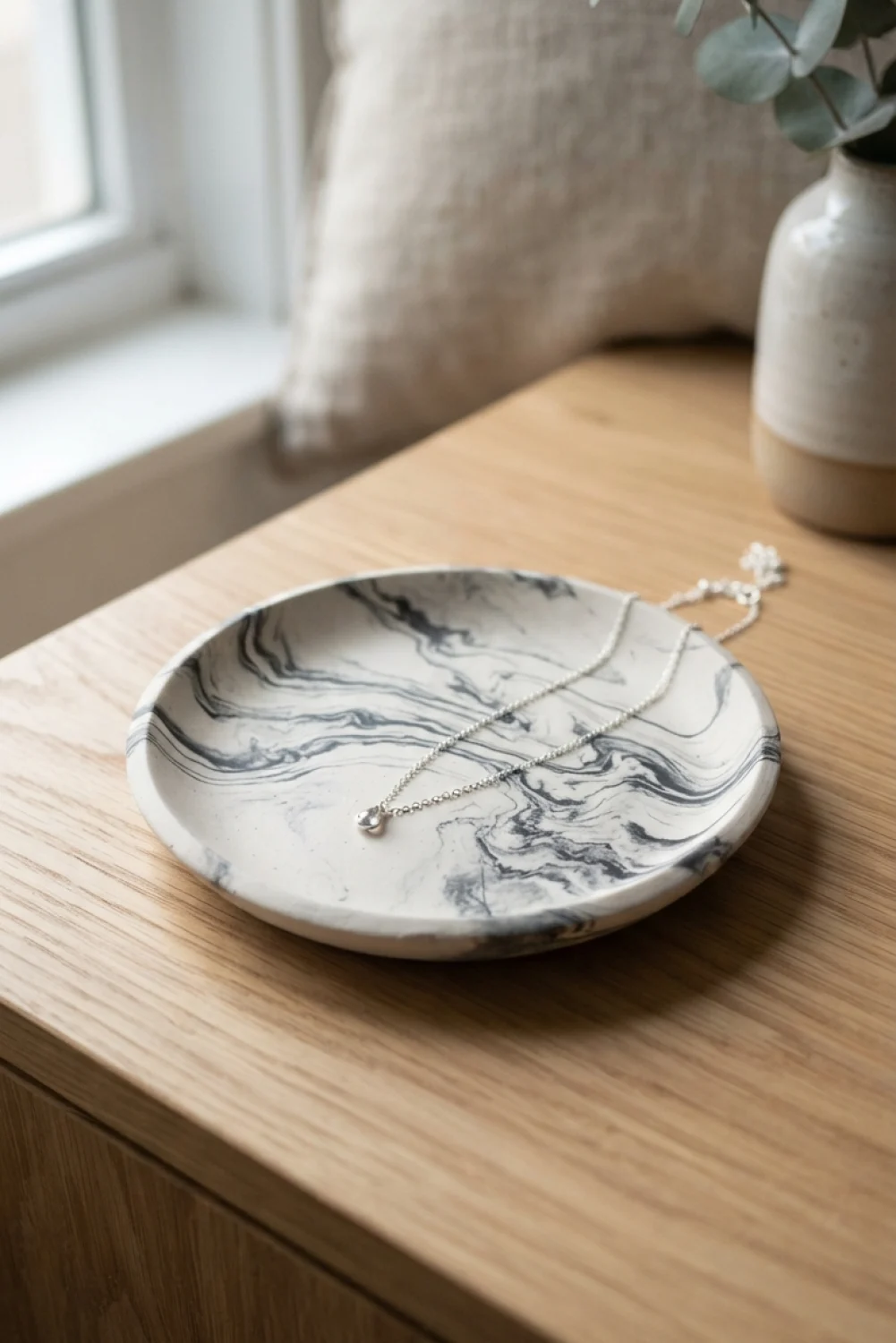 Round marbled black and white air dry clay jewelry dish holding a silver necklace on a wooden table