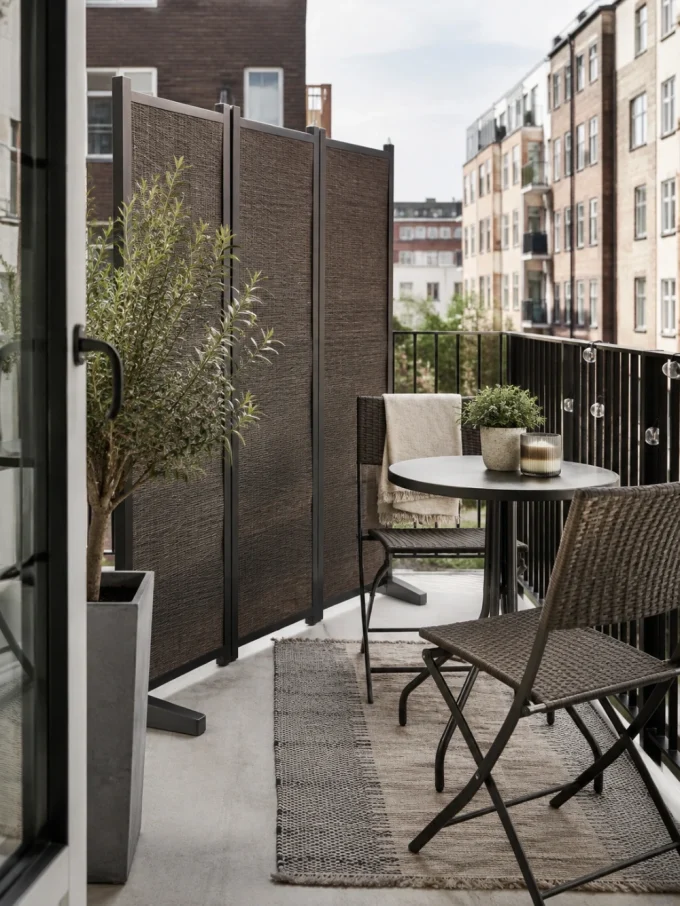 A small balcony with a table, two chairs, and a potted tree