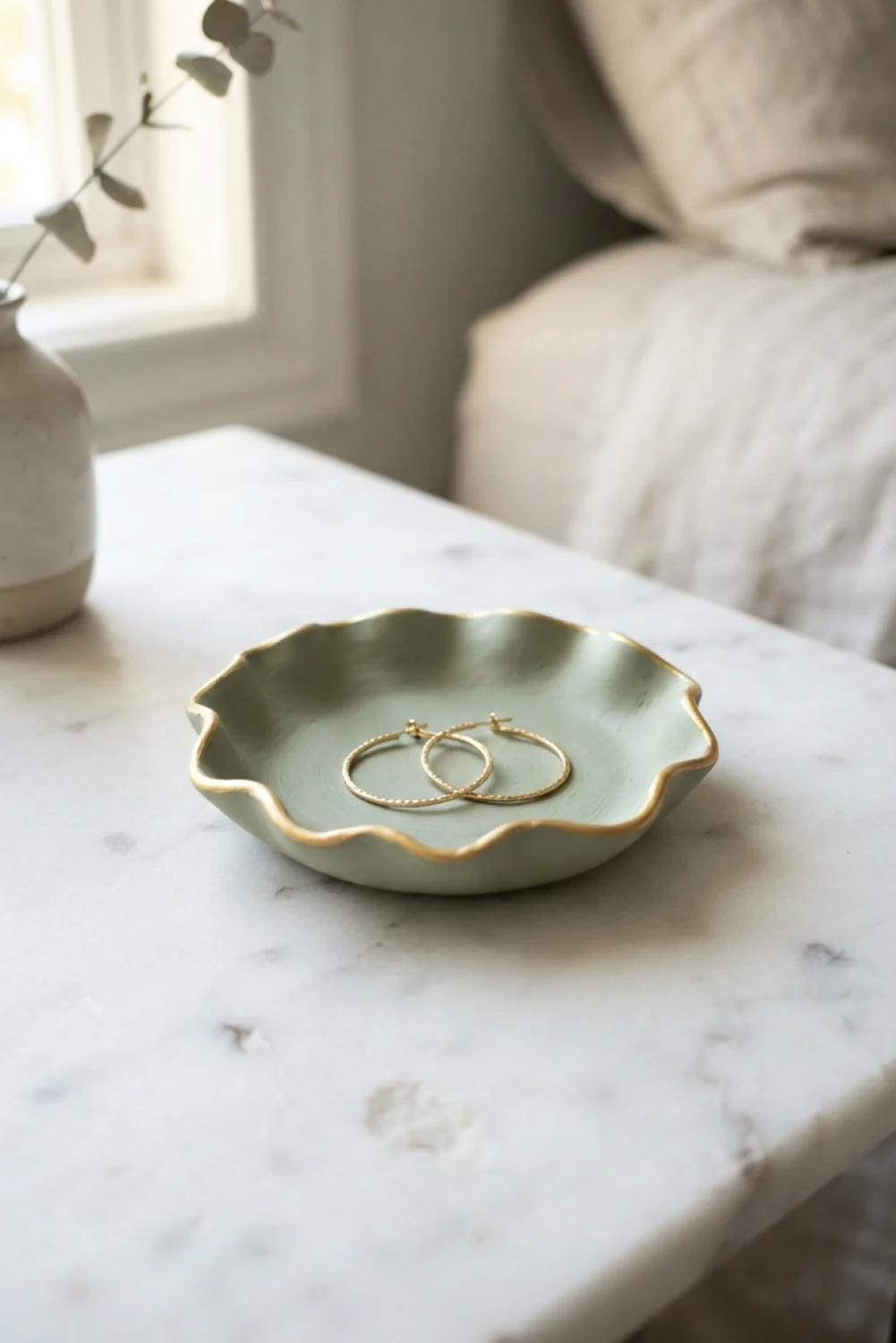 Sage green scalloped air dry clay trinket dish holding gold hoop earrings on a marble table