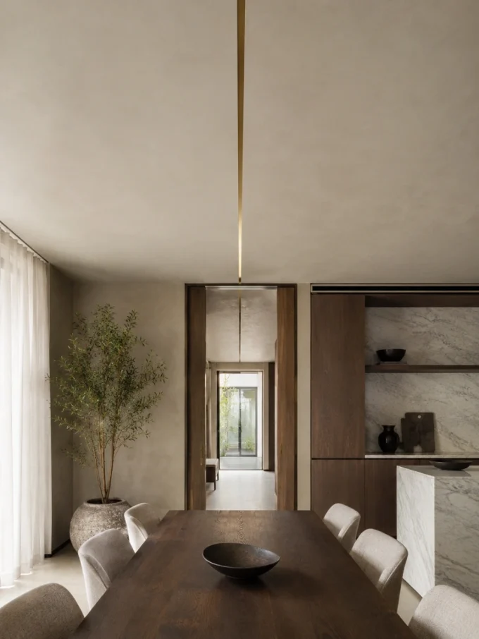 A dining room table with six chairs, a bowl, and a pendant light, with a marble kitchen counter and a potted tree in the background.